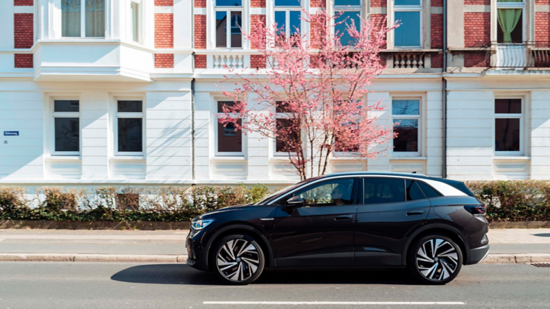 Volkswagen ID.4 aparcado en la calle frente a un árbol en flor y la fachada de un edificio