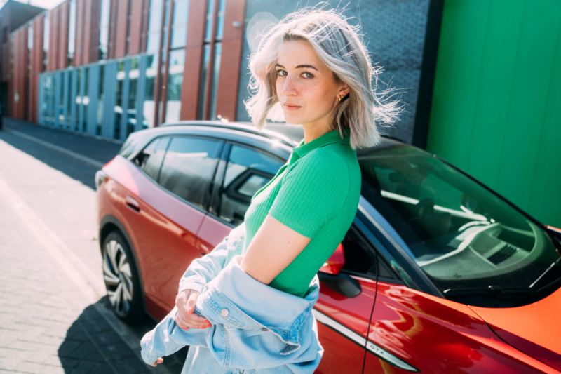 Una chica de verde de pie delante de un Volkswagen ID.4 rojo aparcado en la calle 