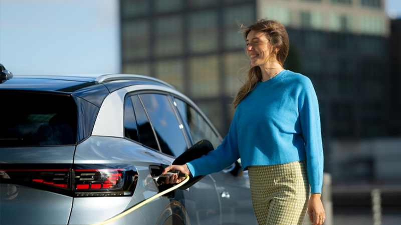 Chica sonriendo conectado un cargador a un Volkswagen ID.