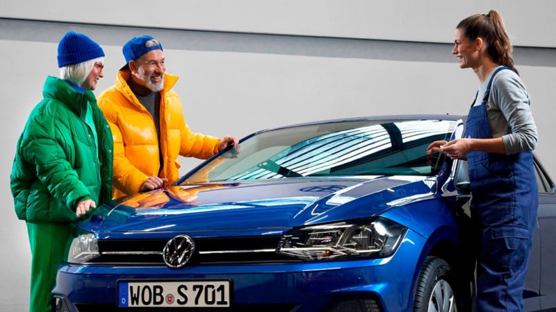 Una pareja de verde y amarillo con una agente de servicio de Volkswagen junto a un coche azul