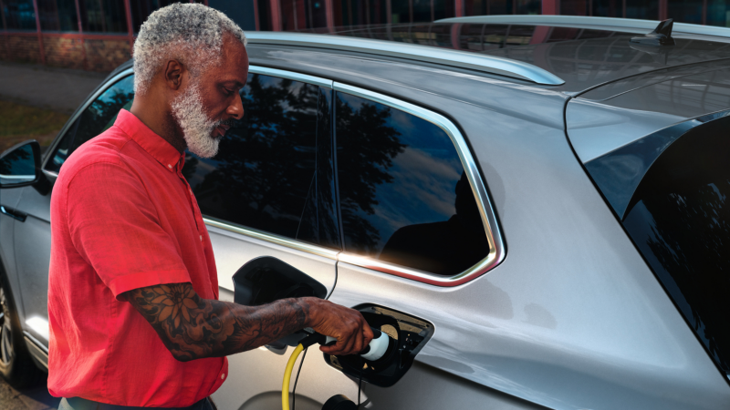 Un hombre de camisa roja conectando un cargador eléctrico a un Volkswagen híbrido