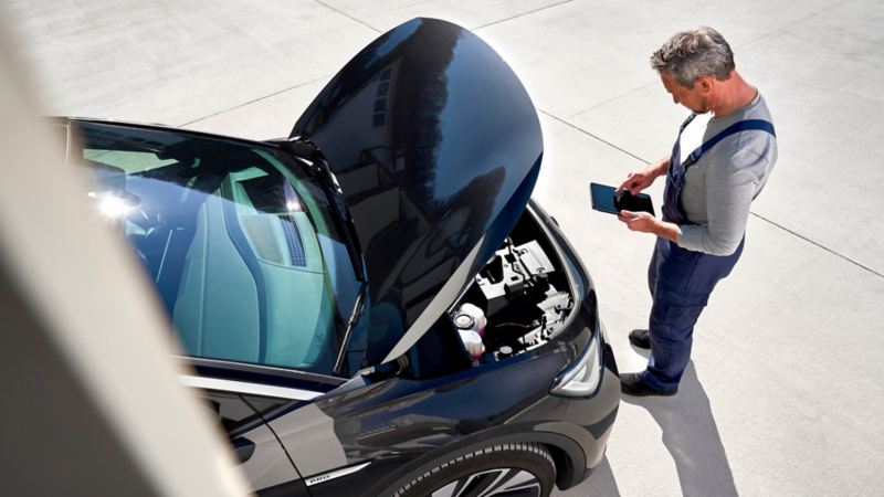 Un mecánico con una tablet delante de un Volkswagen con el capó abierto