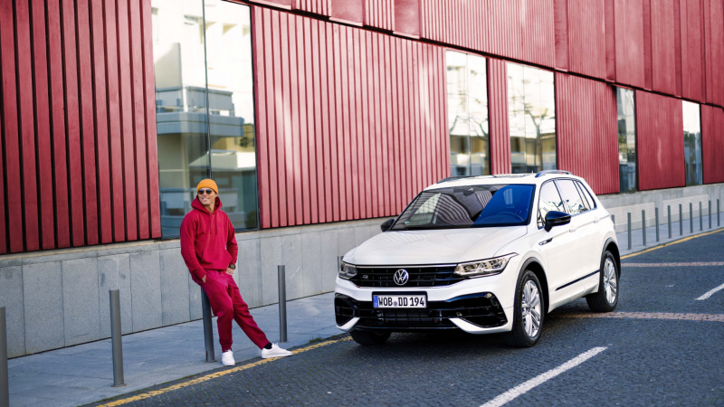 Un chico de rojo delante de un Volkswagen Tiguan blanco aparcado en la calle