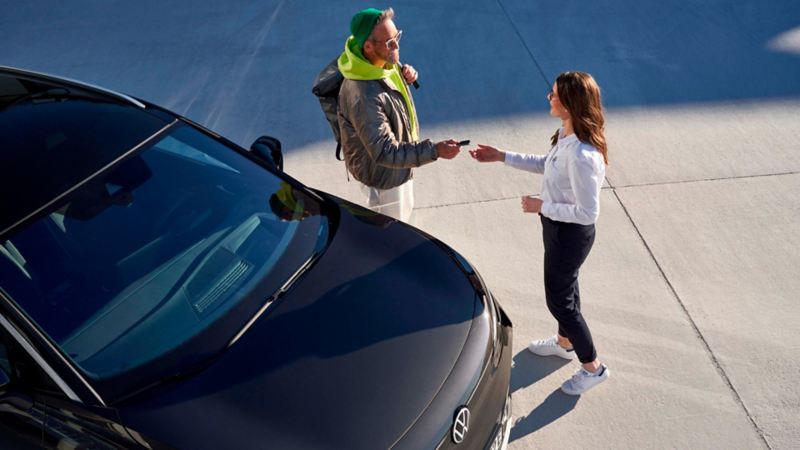 Un chico pasando una llave a una chica junto a un Volkswagen ID: vistos desde arriba
