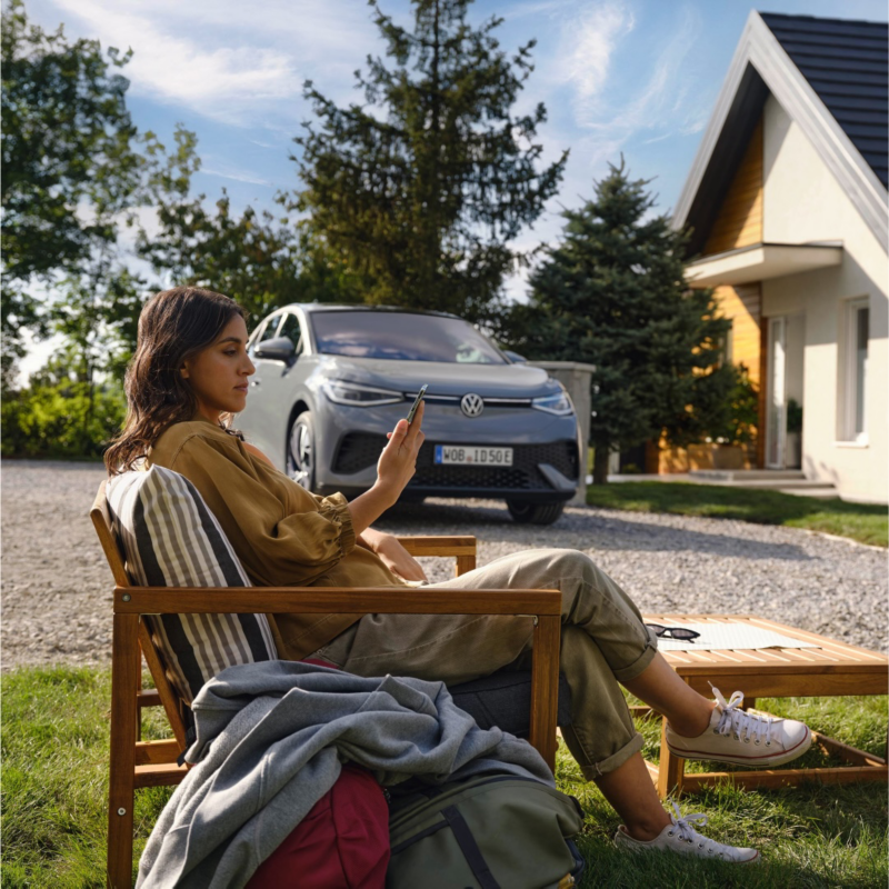 Una chica sentada delante de una casa y un Volkswagen SUV eléctrico