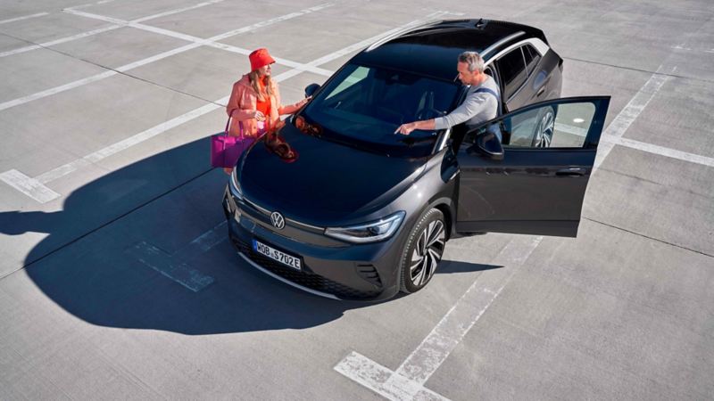 Una mujer y un agente de servicio junto a un Volkswagen ID.4 gris en un parking