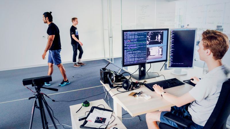 Un informático prueba un sistema de conducción autónoma en un ordenador y personas caminan delante de una cámara