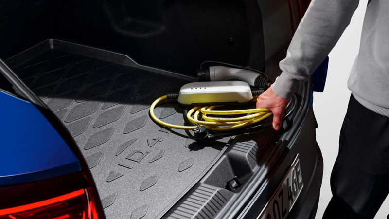 Un hombre sacando el cable de carga del maletero de un Volkswagen azul