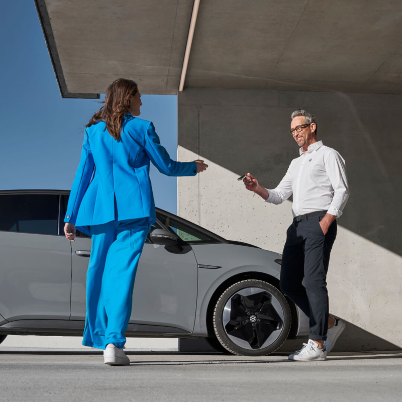 Chica de azul recibiendo la llave de un Volkswagen ID.3 gris de un agente de servicio