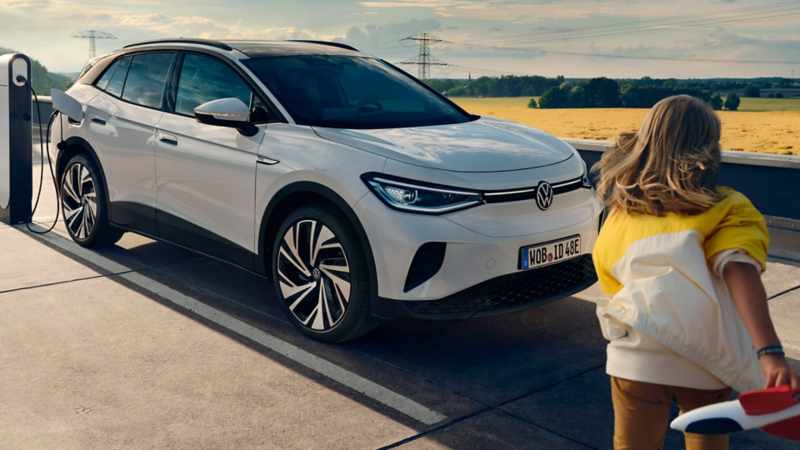 Una niña caminando delante de un Volkswagen ID.4 cargándose en la carretera