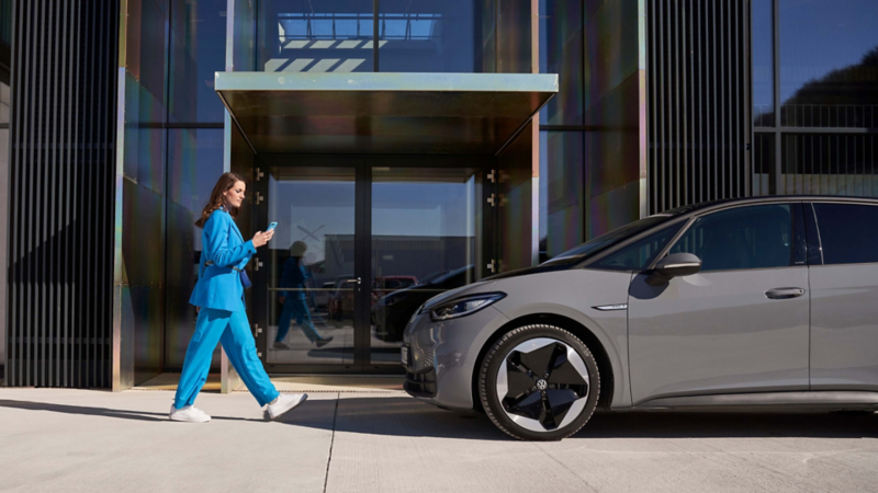 Una chica de azul caminando hacia un Volkswagen ID.3 gris visto de costado