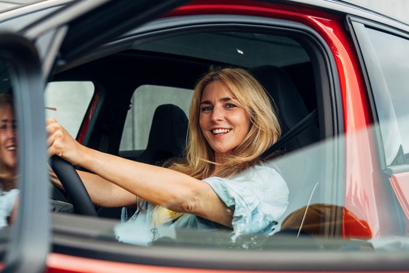 Una chica sonriendo al volante de un Volkswagen vista a través de la ventanilla