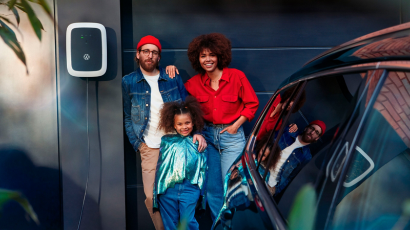 Una familia el la puerta del parking junto a un Wallbox y un coche eléctrico