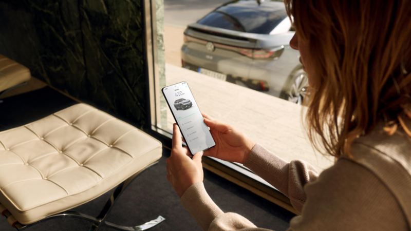 Mujer mirando el móvil sentada en casa y un coche visto a través de la ventana