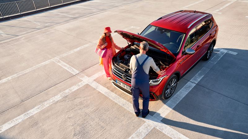 Una chica y un agente de servicio junto a un Volkswagen SUV rojo con el capó abierto