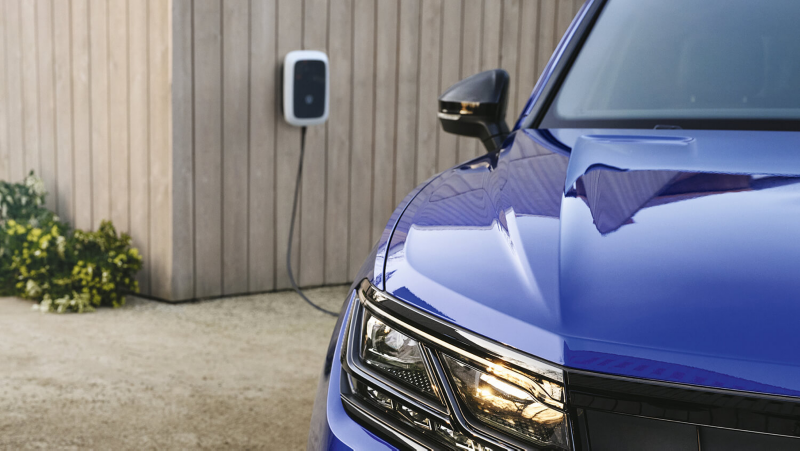 Detalle del faro delantero de un Volkswagen azul y una Wallbox al fondo