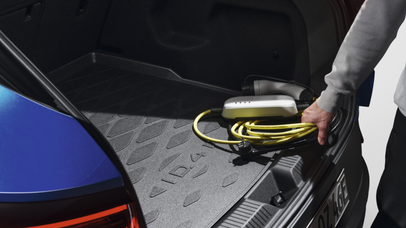 Detalle de un chico cogiendo un cable de carga del maletero de un coche