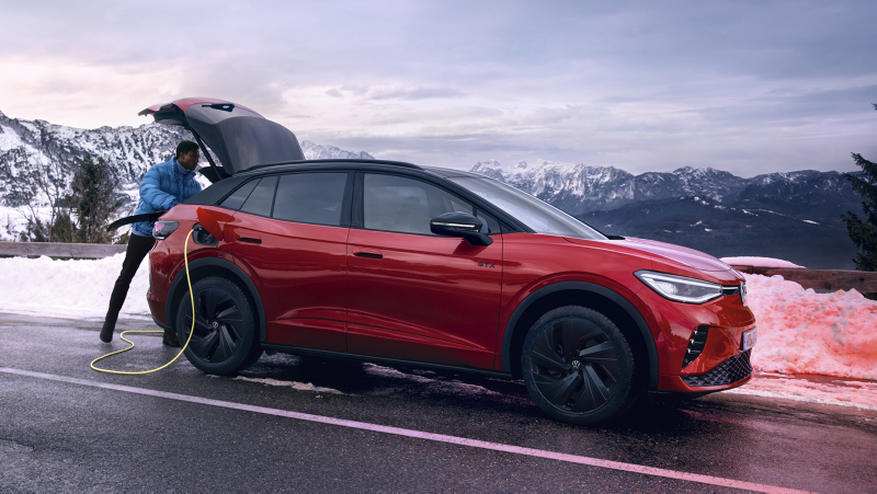 Volkswagen ID.4 rojo en una carretera de montaña con el cable de carga conectado y un hombre mirando el maletero