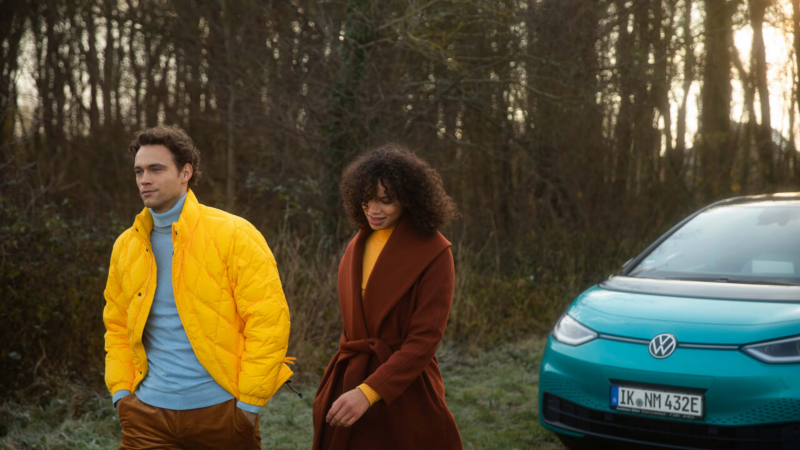 Una pareja caminando en el bosque delante de un Volkswagen ID.3 esmeralda