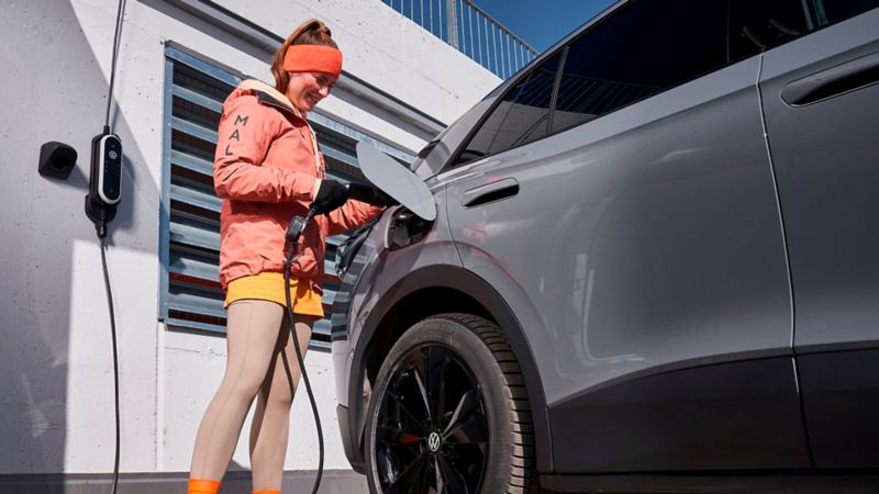 Una chica conectando un cargador de pared a un Volkswagen SUV gris