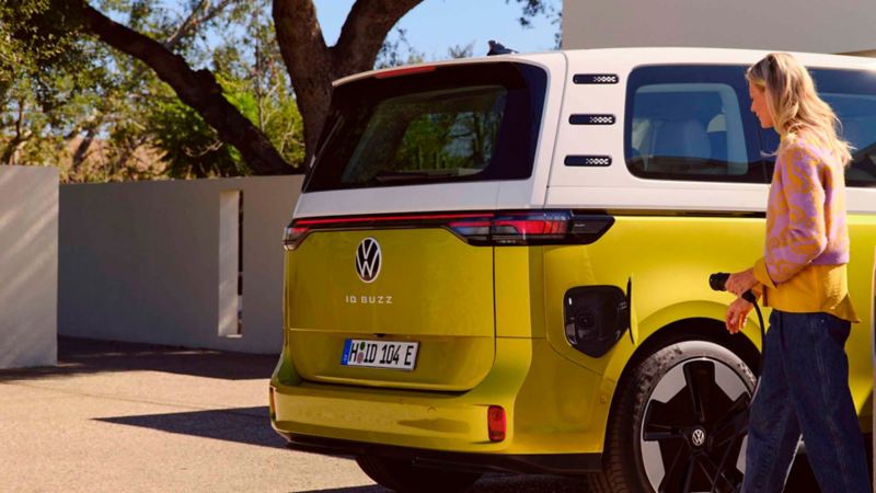 Una chica conectando un cargador eléctrico a un Volkswagen ID: Buzz aparcado en casa