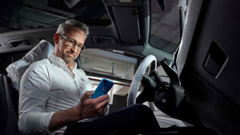 Asistente de servicio de Volkswagen mirando un móvil sentado al volante de un Volkswagen
