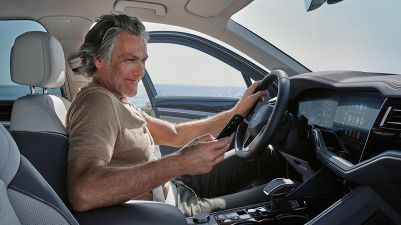 Asistente de servicio de Volkswagen mirando un móvil sentado al volante de un Volkswagen
