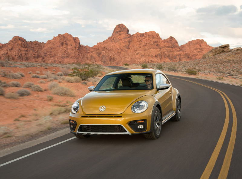Un Volkswagen Beetle amarillo visto de frente en una carretera en el desierto