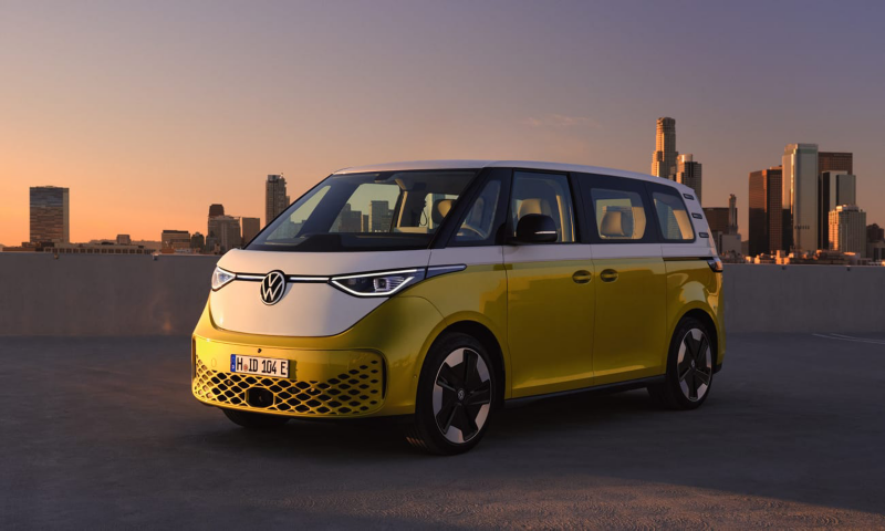 Un Volkswagen ID. Buzz bicolor visto de costado al atardecer con la ciudad de fondo