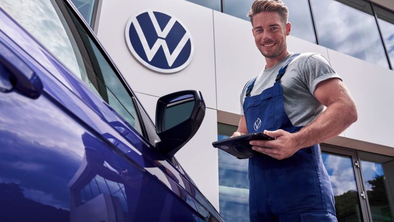 Una agente de servicio Volkswagen junto a un coche azul delante de un concesionario