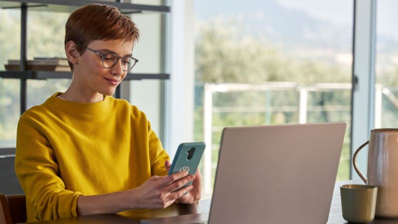 Una mujer con un smartphone delante de un ordenador