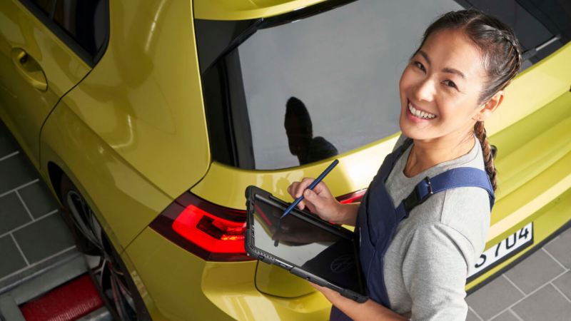 Una agente de servicio Volkswagen sonriendo con una tablet detrás de un Golf 8