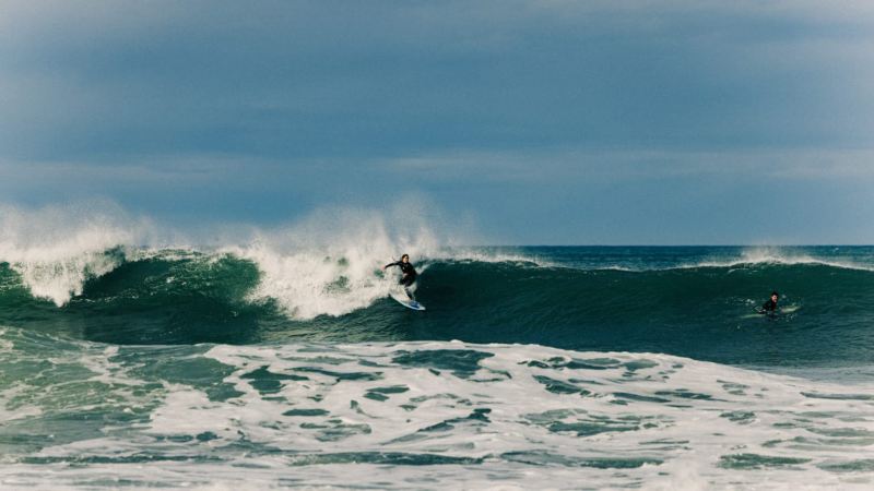 Una chica surfeando una ola con un neopreno The Roadcycled Wetsuit x Blue Banana