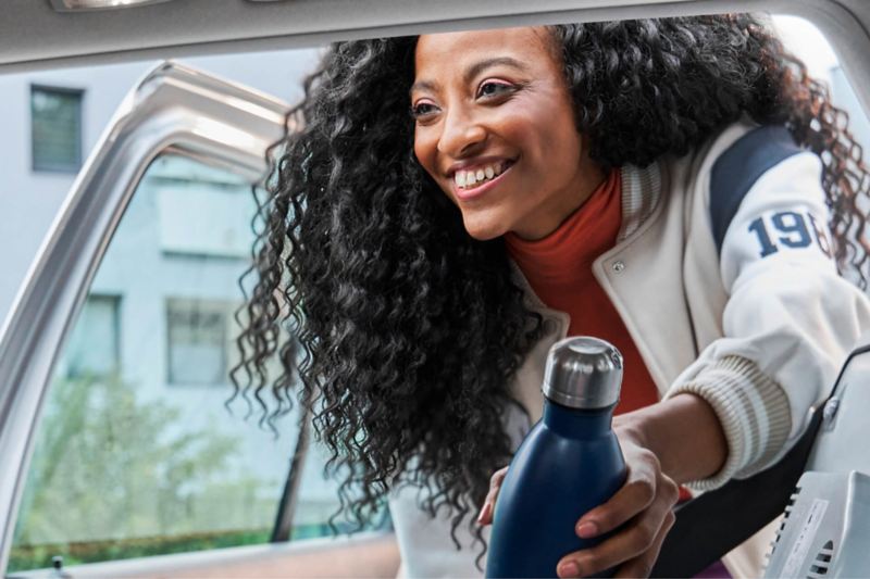 Una mujer cogiendo una botella de Volkswagen desde una hielera en el asiento de atrás