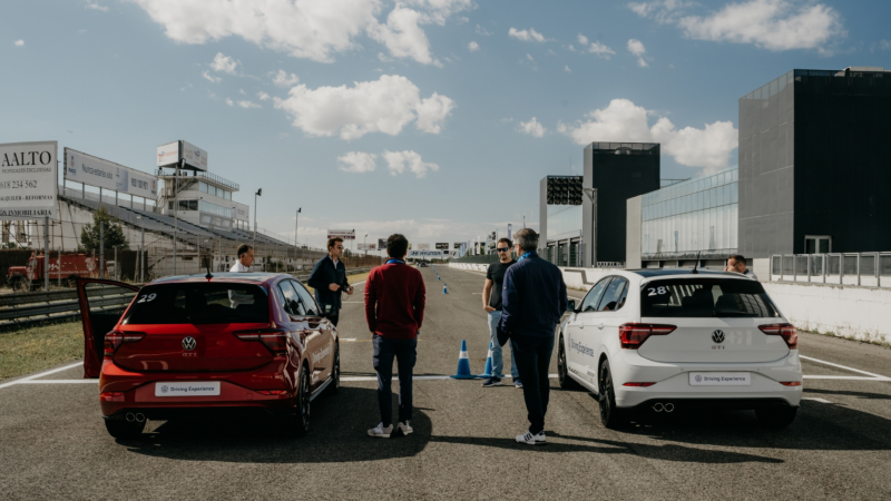 Un grupo de personas junto a dos coches Volkswagen en el circuito cerrado de Jarama