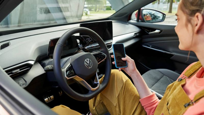 Una chica sentada en un Volkswagen usando el móvil