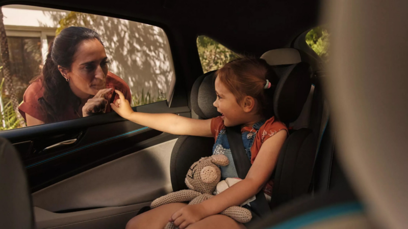 Una niña dentro de un Volkswagen con la madre apoyada en la ventanilla