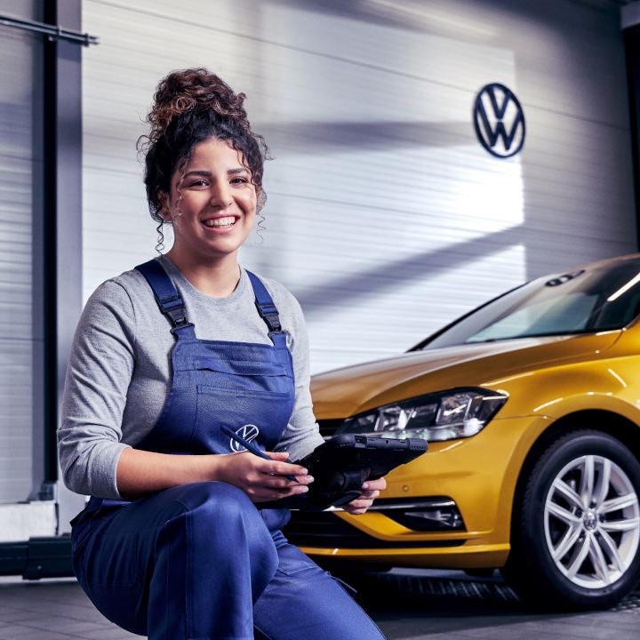 Una agente de servicio Volkswagen sonriendo delante de un coche