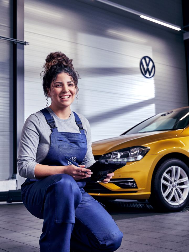 Una agente de servicio Volkswagen delante de un coche amarillo