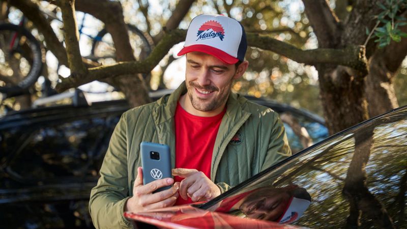 Un chico sujetando un movil al lado de un Volkswagen