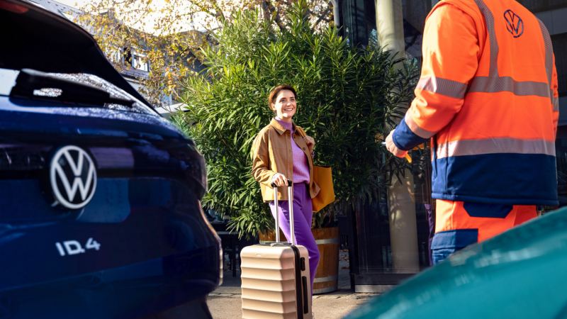 Una mujer con una maleta junto a un ID.4 y un agente de servicio de Volkswagen