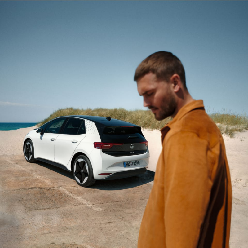 Un chico junto a un Volkswagen ID.3 con el mar de fondo
