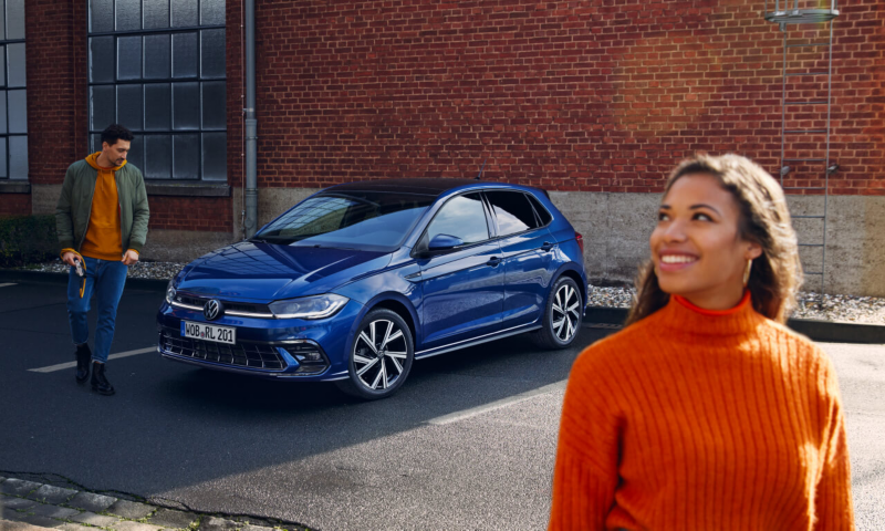 Un chico y una chica junto a un Volkswagen de color azul oscuro