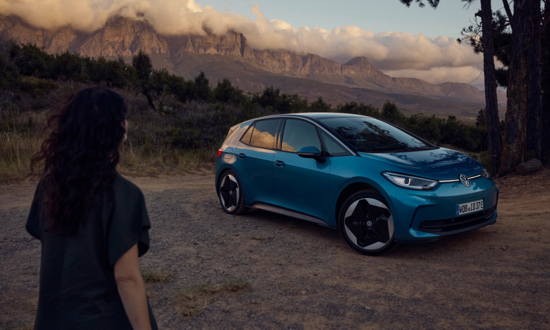 Una chica junto a un Volkswagen de color azul estacionado en una montaña