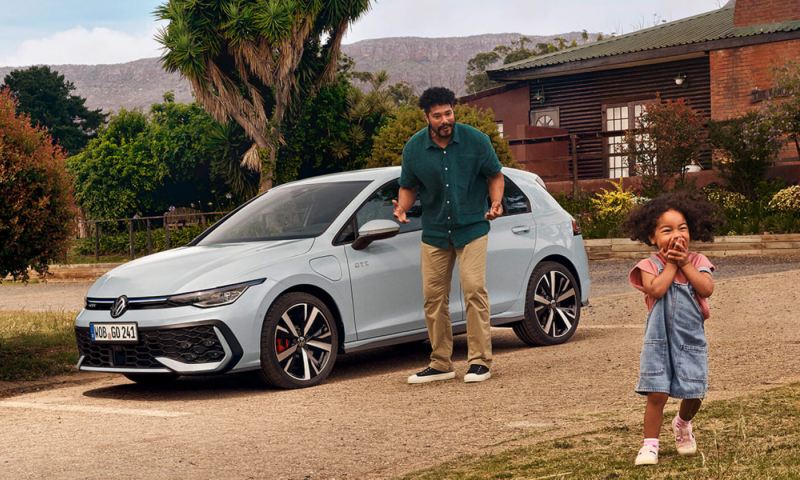 Un padre con una hija junto a un Volkswagen de estacionado frente a una casa