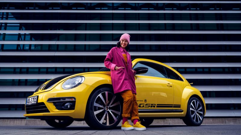 Una chica apoyada en un Volkswagen Beetle amarillo