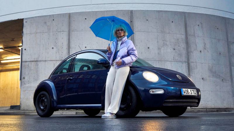 Una chica con paraguas apoyada en un Volkswagen Beetle azul oscuro