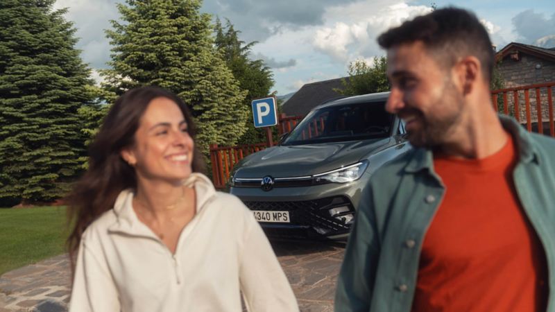 Una pareja delante de un Volkswagen estacionado en una plaza de parking