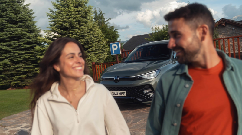 Una pareja delante de un Volkswagen estacionado en una plaza de parking