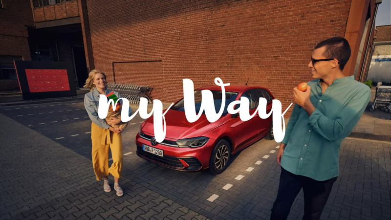 Una pareja saliendo de un supermercado junto a un Volkswagen y el logo de My Way